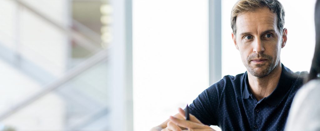 Man in dotted t-shirt talking to someone with a pen in his hand